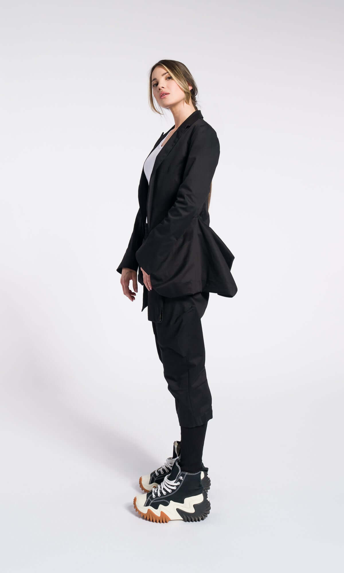 side view of a model in a black blazer, black pants, and platform shoes