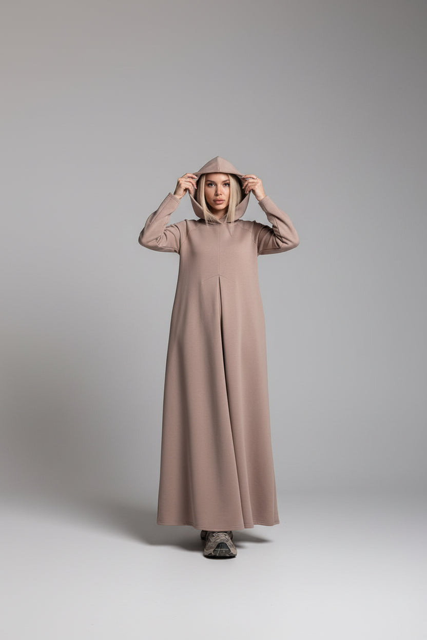 Person wearing a long beige hooded garment in a minimalistic setting