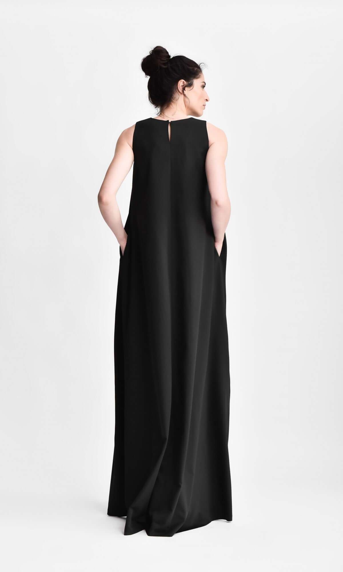 Rear view of a model with her hair in a bun, wearing a sleeveless, floor-length black maxi dress