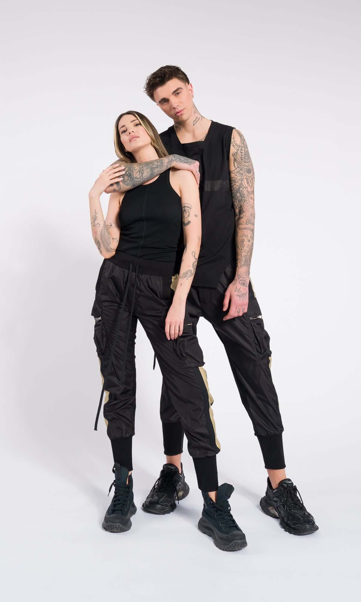 Studio portrait of a couple leaning close, modeling unisex black cargo trousers and sleeveless tops