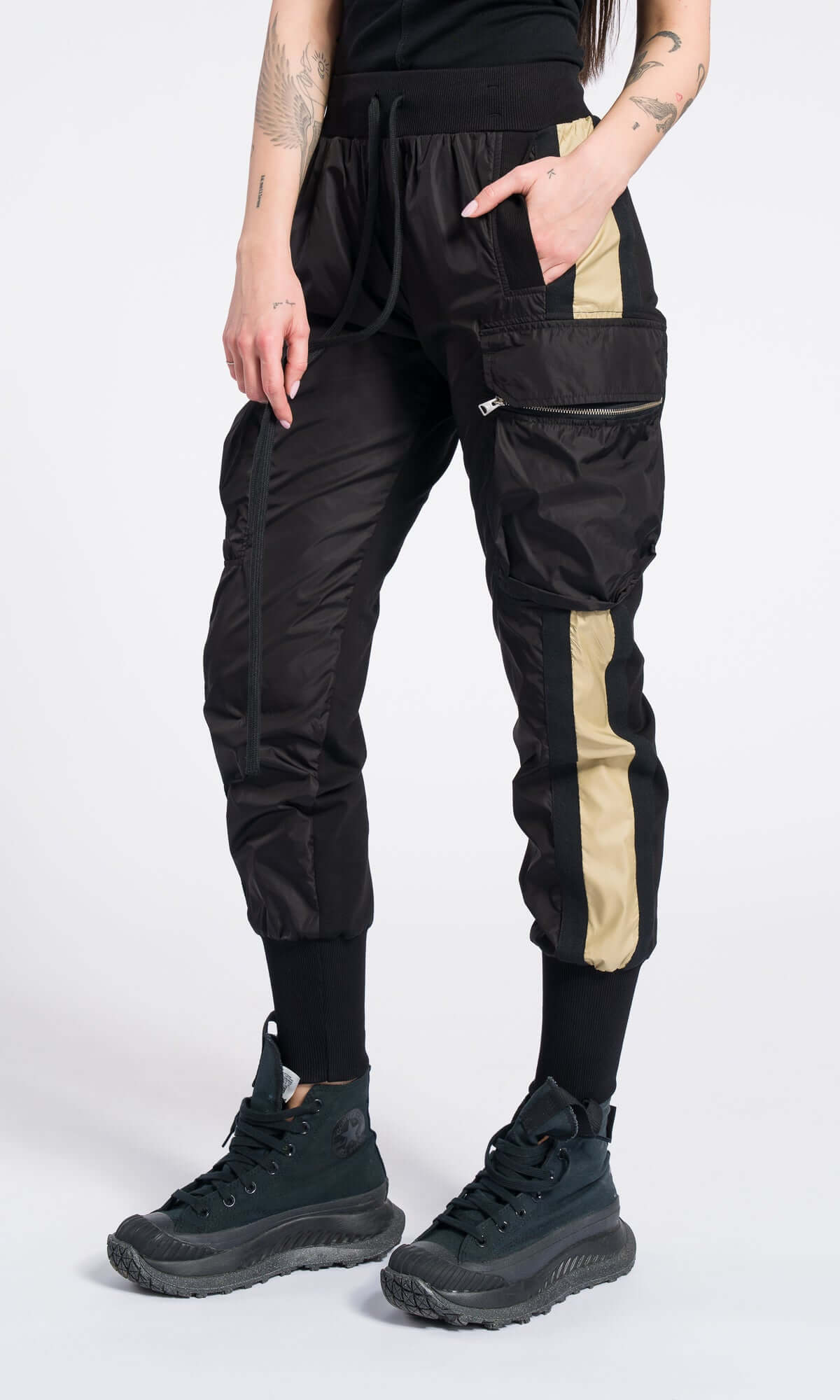 model's hand in the pocket of black cargo pants featuring a vertical tan side stripe.