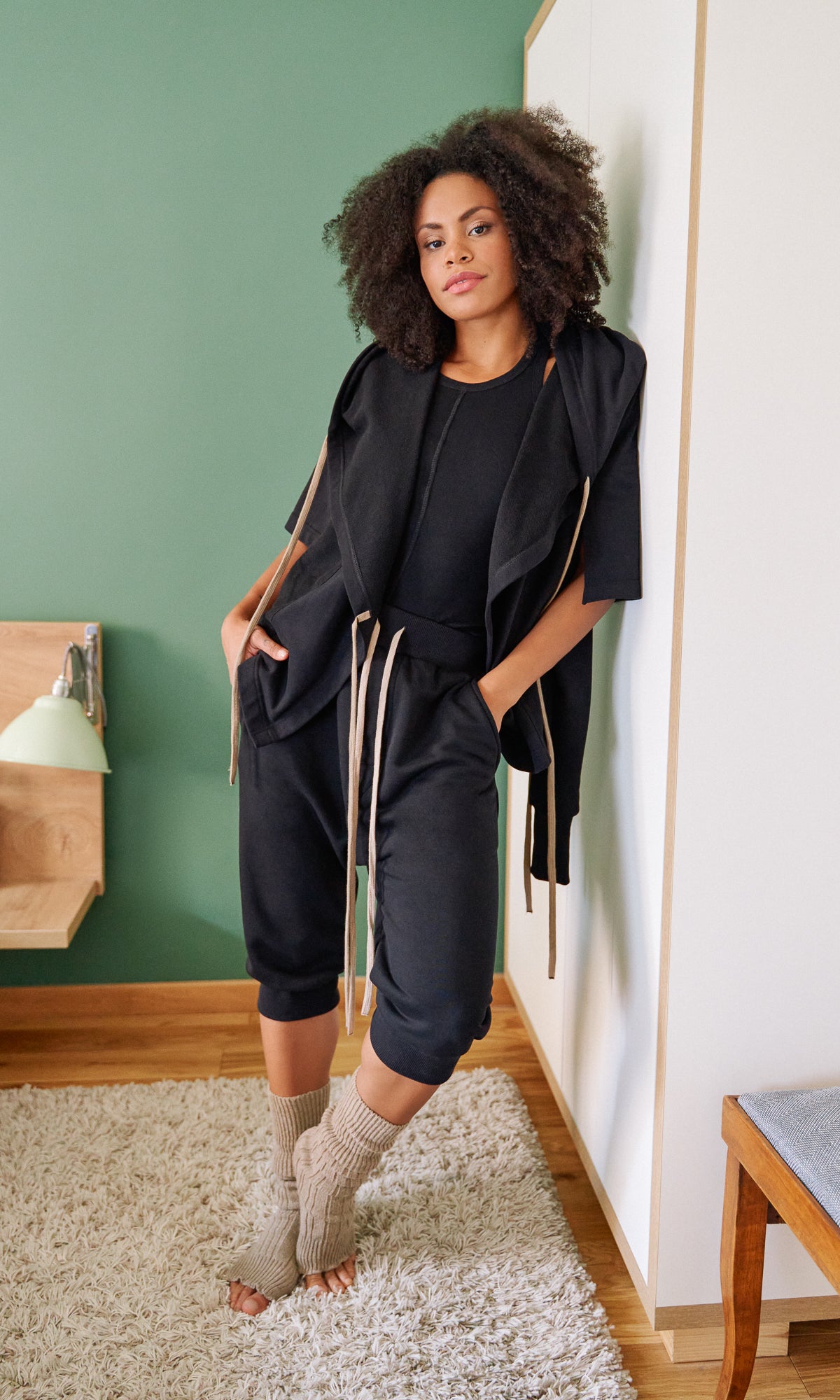 Woman in black outfit standing in a room with green walls and wooden furniture.