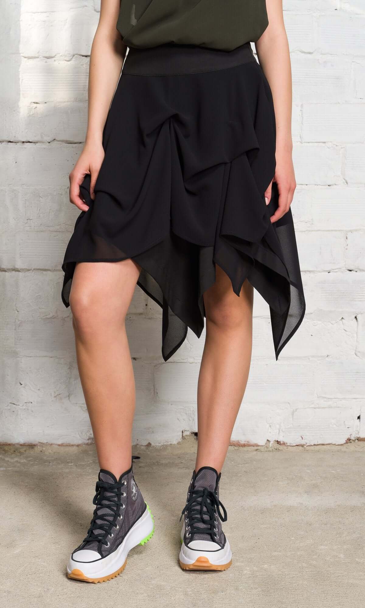 Close-up of a model wearing a tiered, asymmetrical black mesh skirt and high-top sneakers