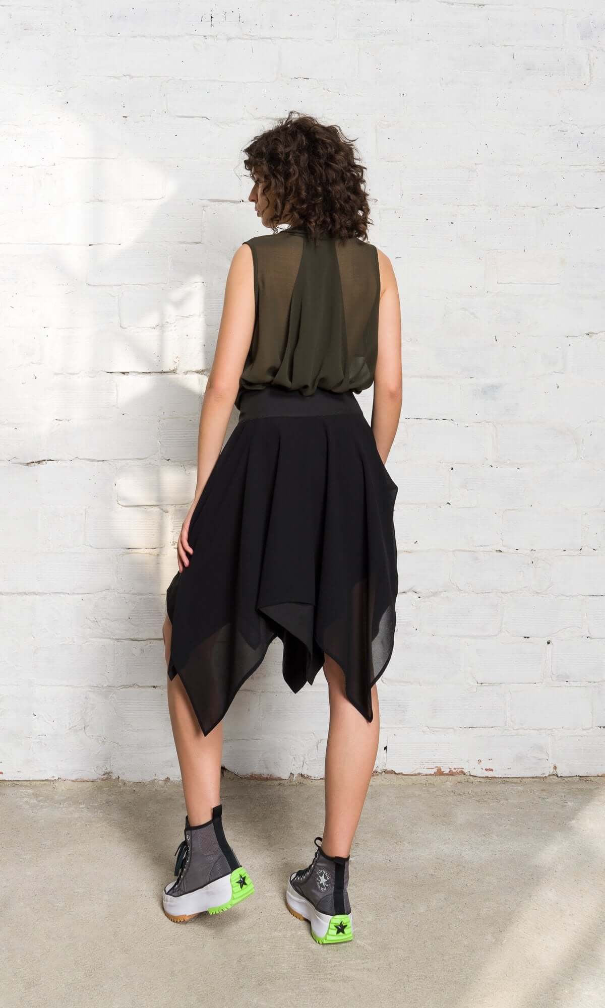 model with curly hair showcasing the back design of a black asymmetrical mesh skirt.