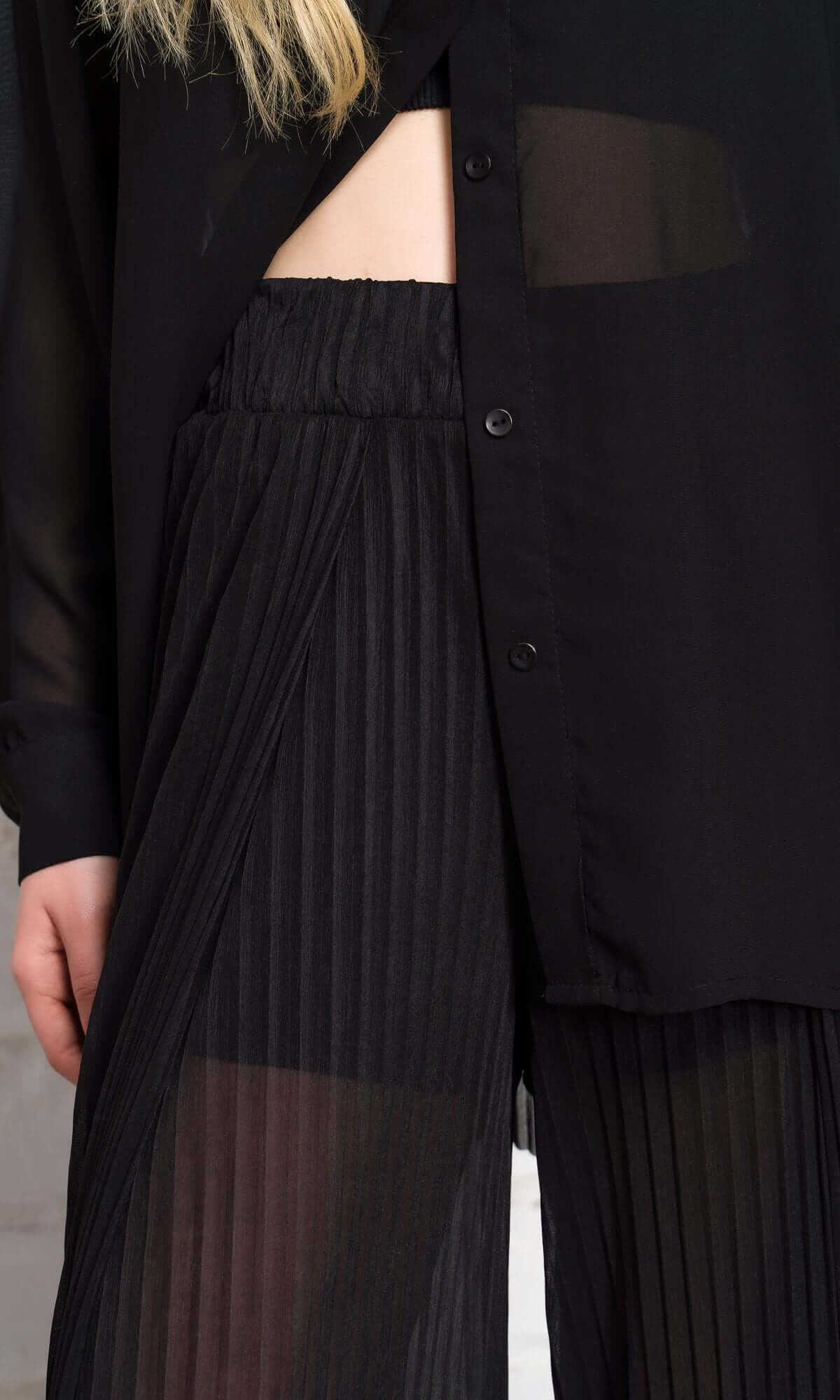 Close-up of sheer black pleated trousers and a matching unbuttoned shirt