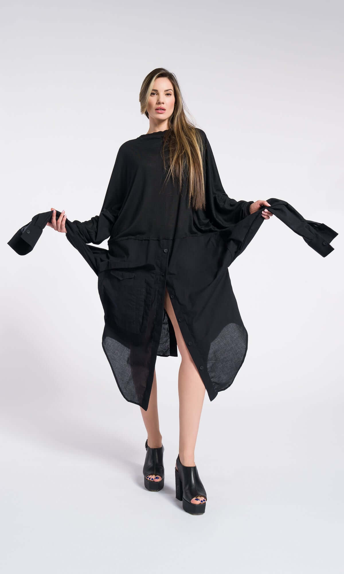 Dynamic shot of a model holding out the fabric panels of a lightweight, oversized black kaftan-style dress.