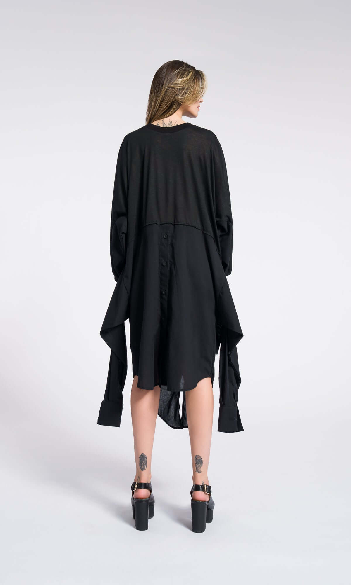 back view of a model showcasing the loose, cascading cape-like silhouette of a black maxi dress.