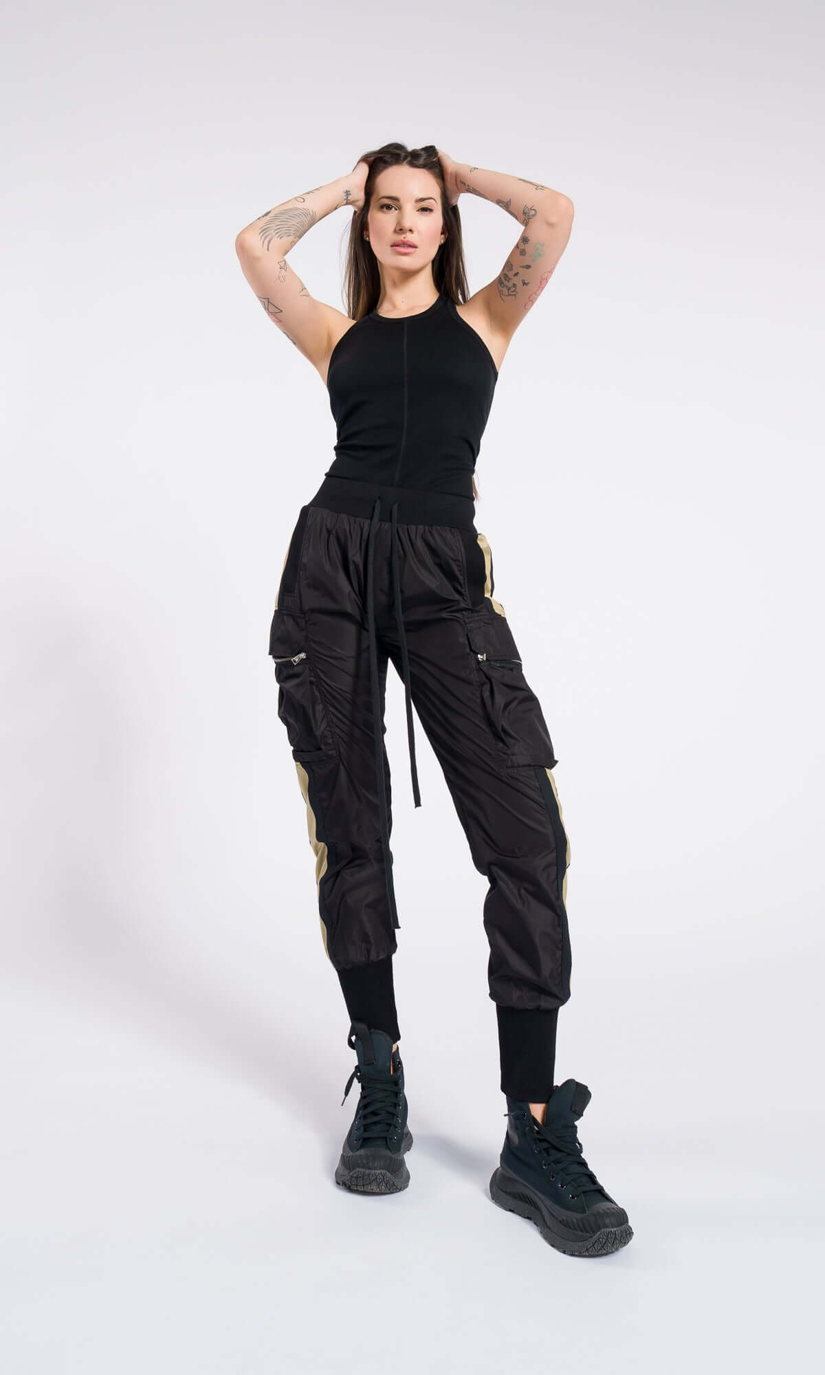 woman posing with both hands behind her head, wearing black cargo pants with a side stripe.