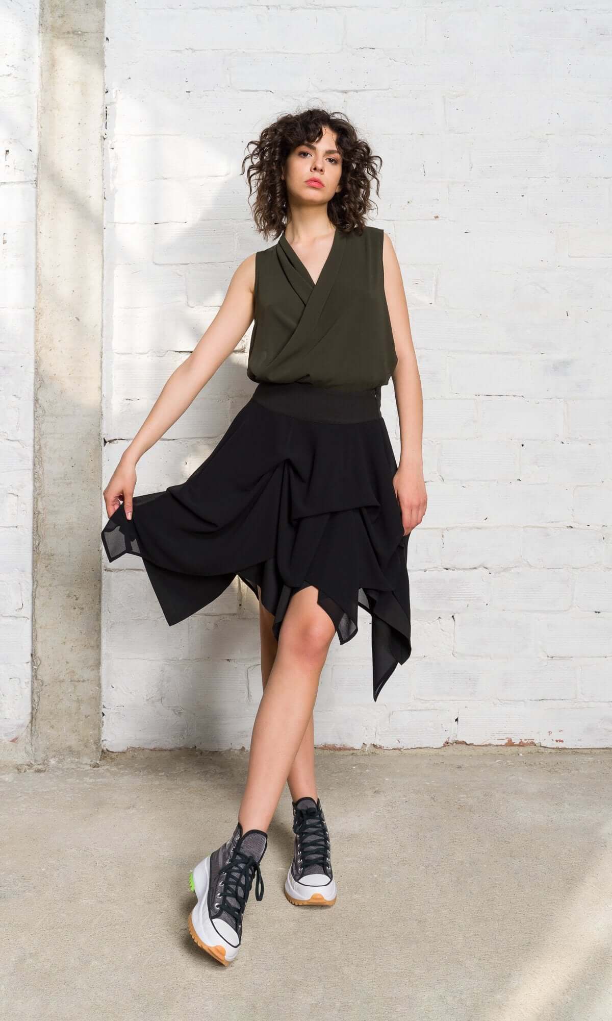 model holding the edges of a flared, layered black handkerchief skirt.