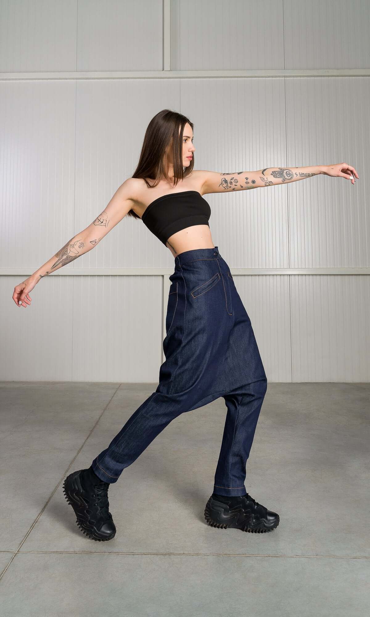 model posing with arms outstretched to the sides, showcasing the movement and flexibility of the dark blue denim harem pants