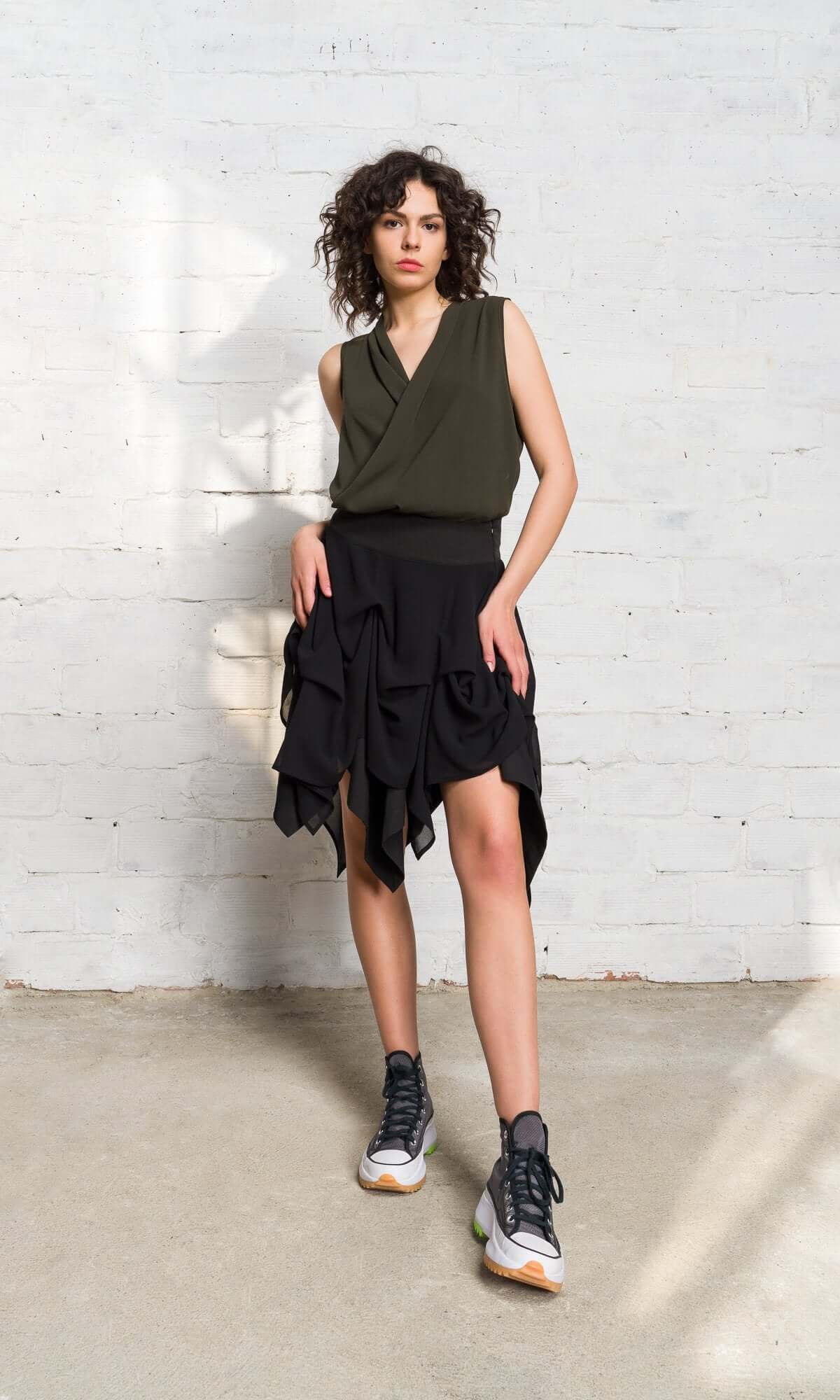 model in an olive green vest and layered black handkerchief-hem skirt.