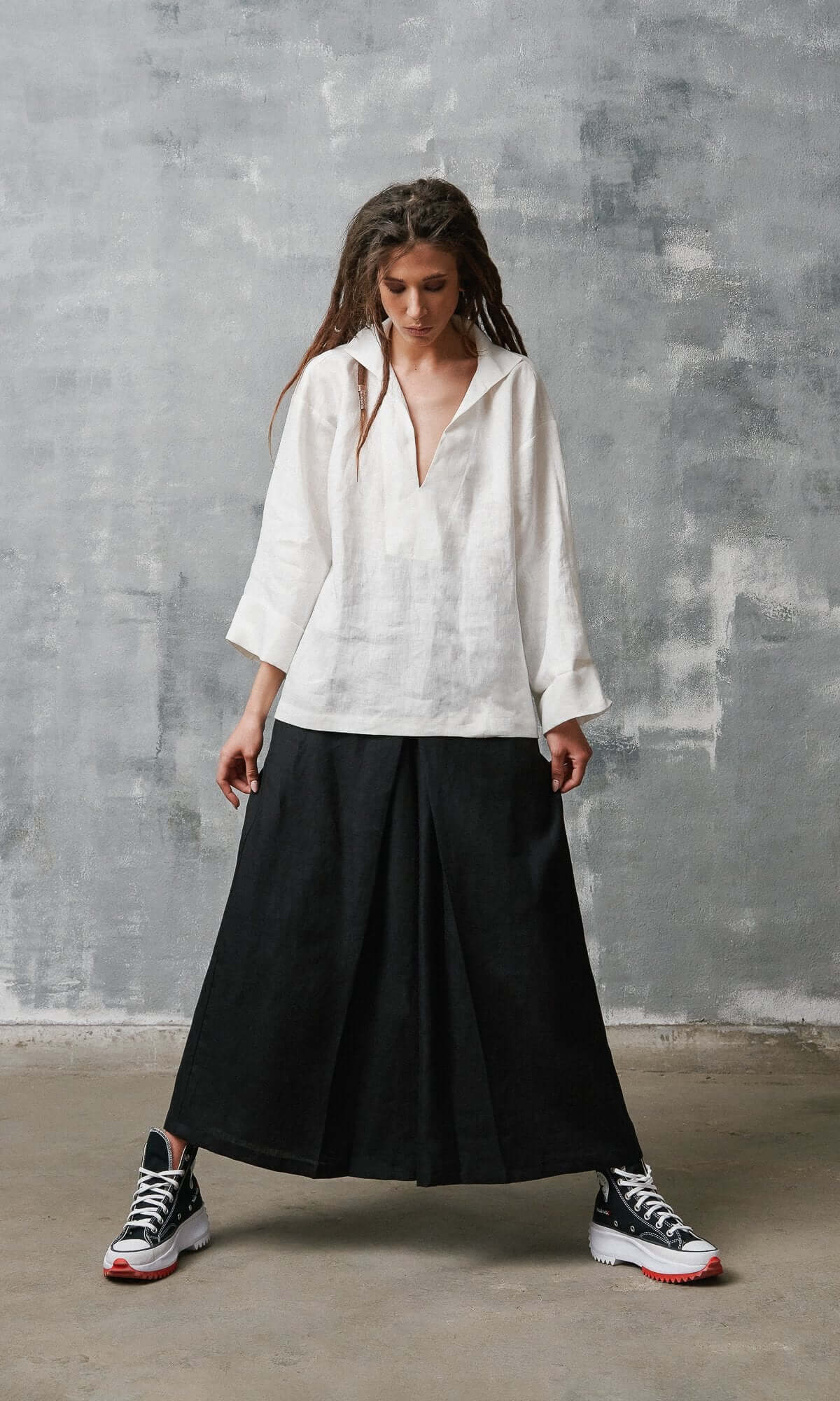 A model wearing a white shirt and black linen skirt pants with an elastic waistband and inverted pleats, standing against a plain background.