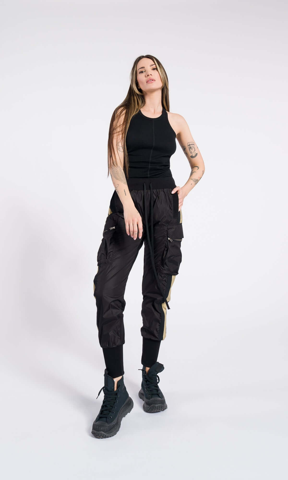 model posing with one hand on her hip, wearing black utility trousers and a black tank top