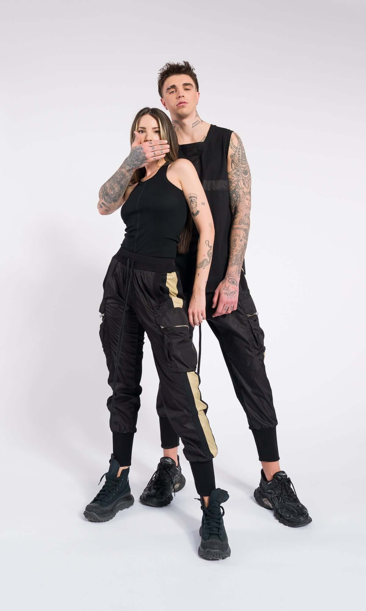 A man and woman standing together in matching black tank tops and cargo pants with vertical tan stripes