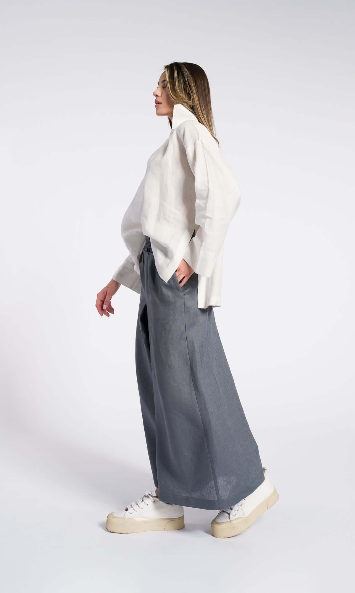 Side view of model wearing a white shirt and grey linen skirt pants with an elastic waistband showing wide led and relaxed fit
