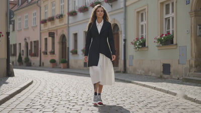 Woman in a black coat and white skirt walking on a cobblestone European street